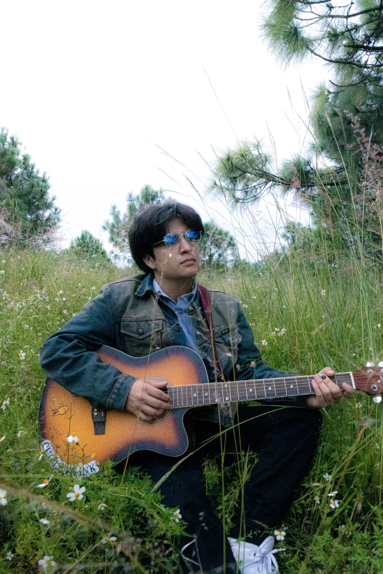 Guille Frank sentado entre pasto y flores con su guitarra acústica